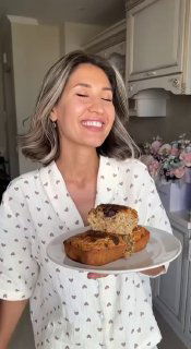 Женщина держит тарелку с кусочками воздушного ПП бананового кекса на кухонном фоне, на кексе — тёмный шоколад.