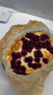 Вид сверху на домашнюю творожную запеканку с вишней: ягоды распределены по поверхности, корочка золотистая, запечена в форме на пергаменте