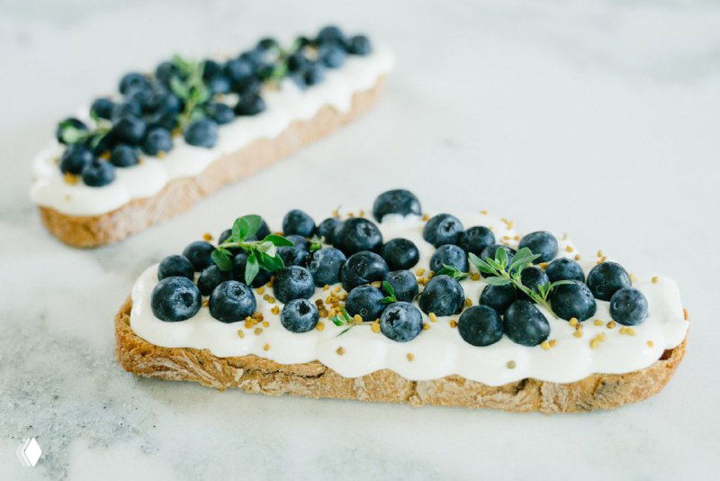 Длинные тосты с творожным кремом и свежими голубиками на светлом фоне — вариант ПП-десерта или перекуса без сахара.