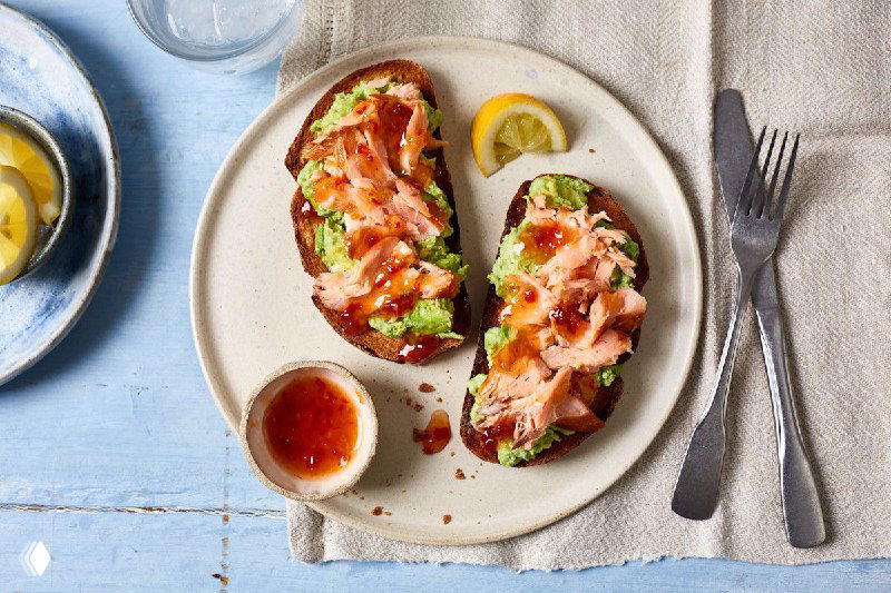 Две брускетты с лососем и зеленью на тарелке рядом с соусом и лимоном — питательный вариант с омега-3 и белком.