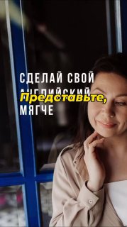 Улыбающаяся женщина в деловом образе у окна на фоне синих рам; фотография иллюстрирует мягкий, вежливый тон общения в деловом английском.