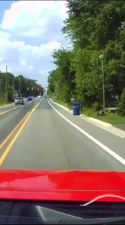 Съёмка с автомобиля: красный капот внизу кадра, прямая загородная дорога с разметкой, обочины в зелёных деревьях и небо с облаками; нейтральный фон для поста.