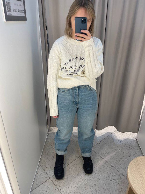 Фото примерки: женщина в светлом свитере и голубых джинсах делает селфи в примерочной — полный рост, показывает реальную посадку и длину джинсов в комплекте.