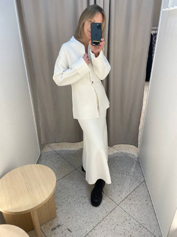 Примерка: женщина в белом трикотажном костюме — жакет и миди-юбка, снимок в примерочной демонстрирует целостность образа и посадку комплекта в полный рост.