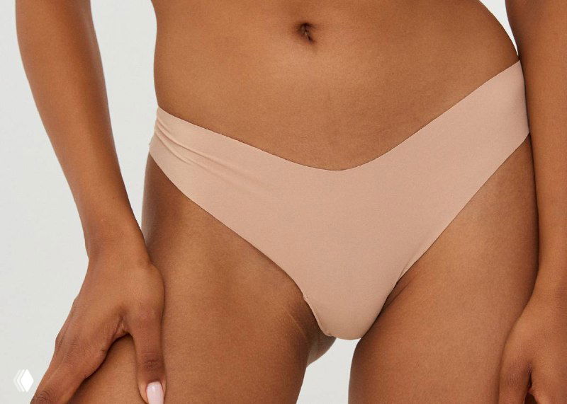 Модель в бежевых V‑образных трусах, акцент на линию бёдер и минимальную видимость под облегающей одеждой.
