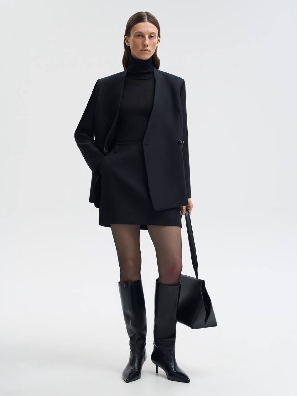 Модель в чёрном пальто и высоких сапогах, сочетание текстуры и посадки создаёт статусный образ без ярких элементов.