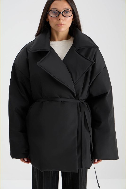 Чёрная стёганая короткая куртка с поясом на модели — расслабленный укороченный фасон для межсезонья в капсуле верхней одежды.