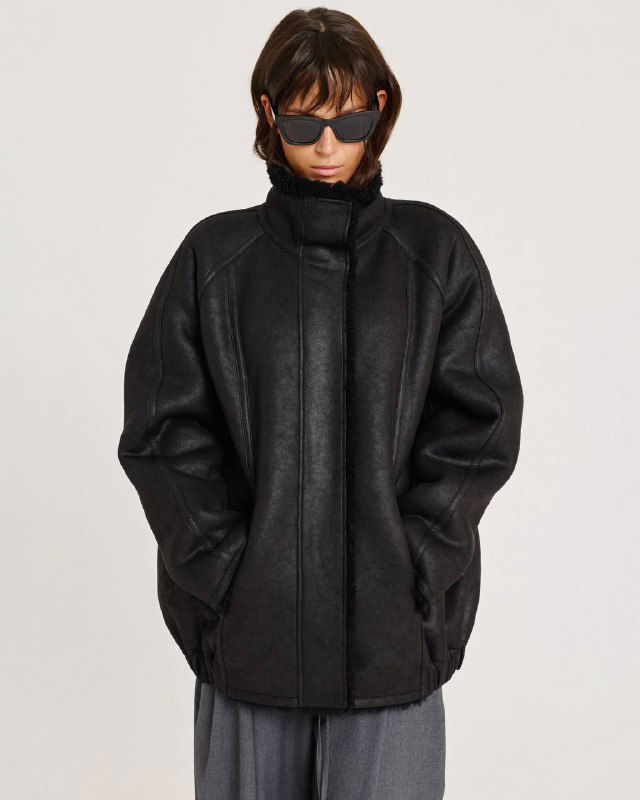 Чёрная дублёнка/куртка объёмного силуэта на модели, шероховатая текстура и высокий воротник — пример расслабленного фасона пальто/дублёнки.