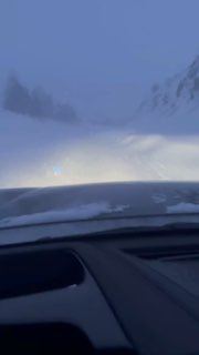Вид из салона автомобиля на заснеженный горный перевал в метель: дорога почти исчезает за сугробами и перемётами, видна приборная панель.