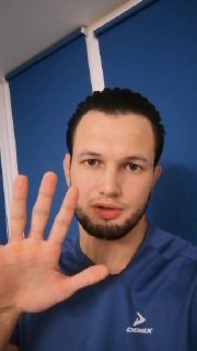 Крупный план лица тренера в спортивной футболке, поднятая ладонь в кадре — жест внимания и обращение к подписчикам о курсе по стойкам.