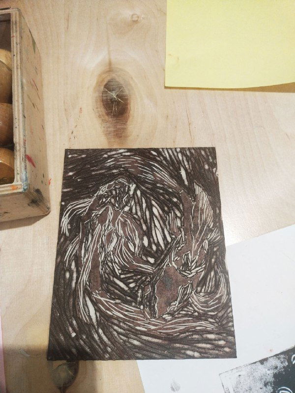 Крупный план тёмной вырезанной пластины с рельефным спиралевидным рисунком — подготовленная поверхность для печати оттиска.