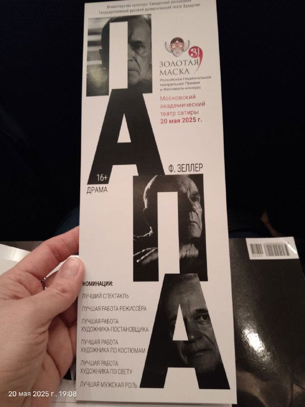 Рука держит буклет фестиваля «Золотая маска» с вертикальным оформлением слова «ПАПА» и логотипом премии, крупный план.