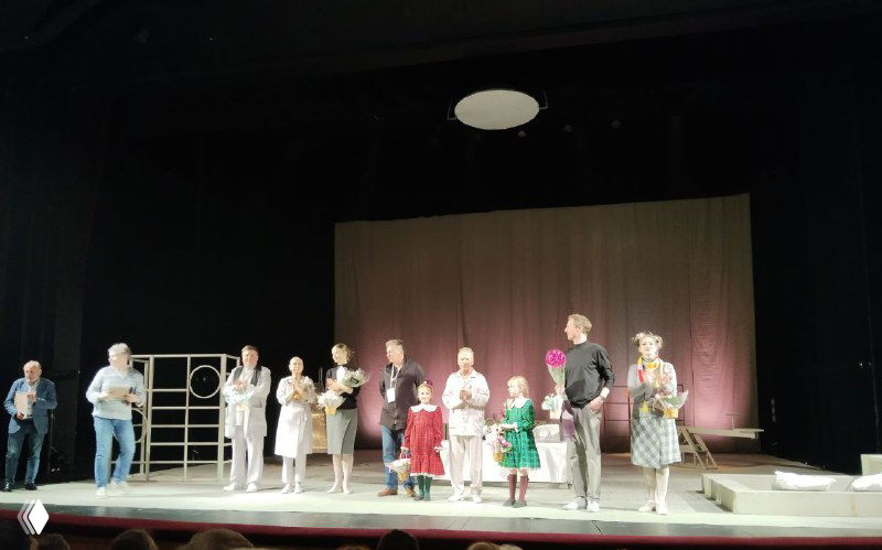 Антракт или финал: на сцене выстроены актёры и организаторы, вручение цветов и аплодисменты публике в зале.