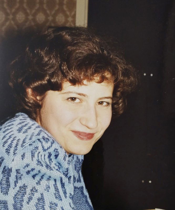 Крупный план женщины в тёплом шарфе, улыбается; снимок в помещении, начало карьеры, портретный формат, атмосферный личный кадр.