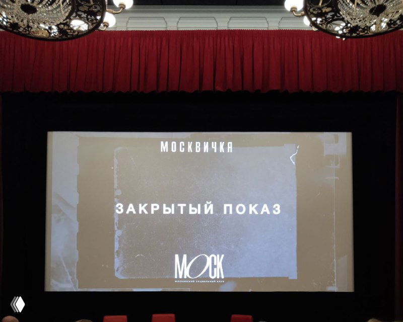 Экран в зрительном зале во время закрытого показа: проекторное изображение с надписью «МОСКВИЧКА» и строкой «ЗАКРЫТЫЙ ПОКАЗ» на фоне красного занавеса.