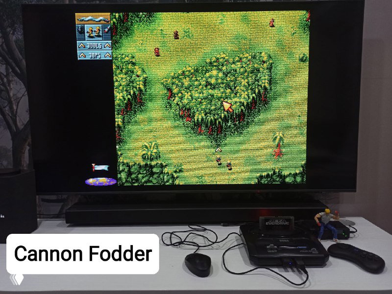 Скрин и игровая сцена Cannon Fodder, показанная на телевизоре, рядом видны SEGA Mega Drive и подключённые мышки — пример официальной поддержки игры.