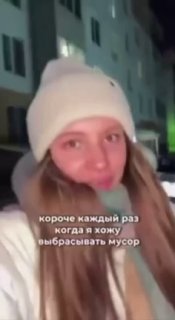Вертикальное видео на улице: молодая женщина в шапке записывает ролик на фоне жилого дома, на экране текст о привычке выбрасывать мусор и долгах.