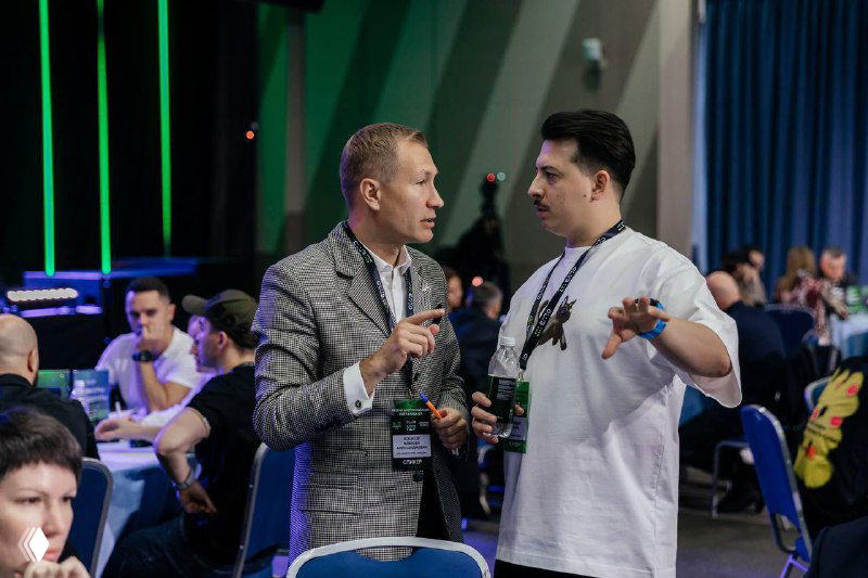 Обсуждение между участниками слёта: два мужчины в диалоге за столом, зрители и формат групповой работы конференции.