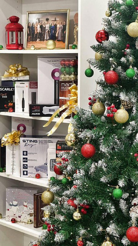 Полка с подарочными наборами и бытовой техникой рядом с украшенной рождественской ёлкой — варианты призов и подарков по акции для партнёров.