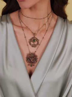 Детальный крупный план декольте с двумя подвесками разного размера и фактуры, одна из которых превращается в брошь‑аксессуар, акцент на деталях отделки.