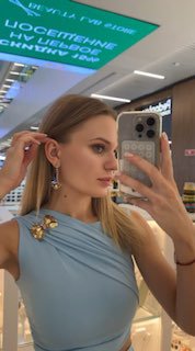 Портретное селфи в бутике: девушка примеряет серьги и показывает боковой профиль вместе с подсветкой витрины и украшениями.
