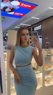 Полный рост в зеркало: женщина в голубом комплекте украшений стоит перед витриной бутика с подсветкой и дисплеем ювелирных товаров.