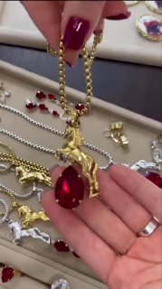 Кадр видео: демонстрация крупного золотого кулона-лошади с большим красным каплевидным кристаллом в руках консультанта, презентация дизайна.