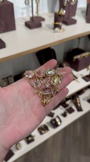 Крупный план: рука держит набор прозрачных и золотистых кристаллов на фоне полок с украшениями и браслетами в магазине Rosone, демонстрация материалов.