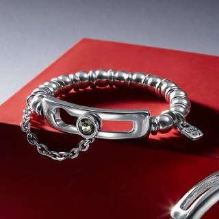 Массивный серебристый браслет с декоративной застёжкой и цепочкой, представленный на тёмно-красном фоне — украшение в минималистичном стиле.