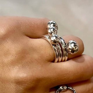 Крупный план сложенного набора серебристых колец с шариками на пальце модели; текстура металла и отражения на поверхности.