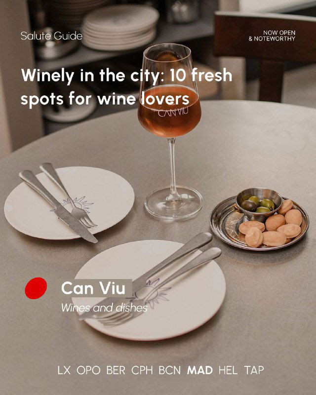 Simple table setting with a glass of amber wine, small plates and olives, illustrating wine-forward small-plates dining in a neighbourhood spot.