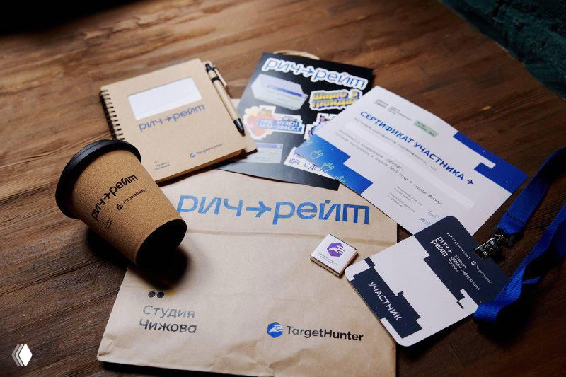 Разложенные на столе фирменные материалы мероприятия: блокноты, бейджи, стикеры и бумажный стакан с логотипом — элементы офлайн-опыта участников.