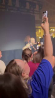 Зал конференции: аудитория снимает сцену на смартфоны — размытый кадр с поднятыми руками и выступающим на сцене.