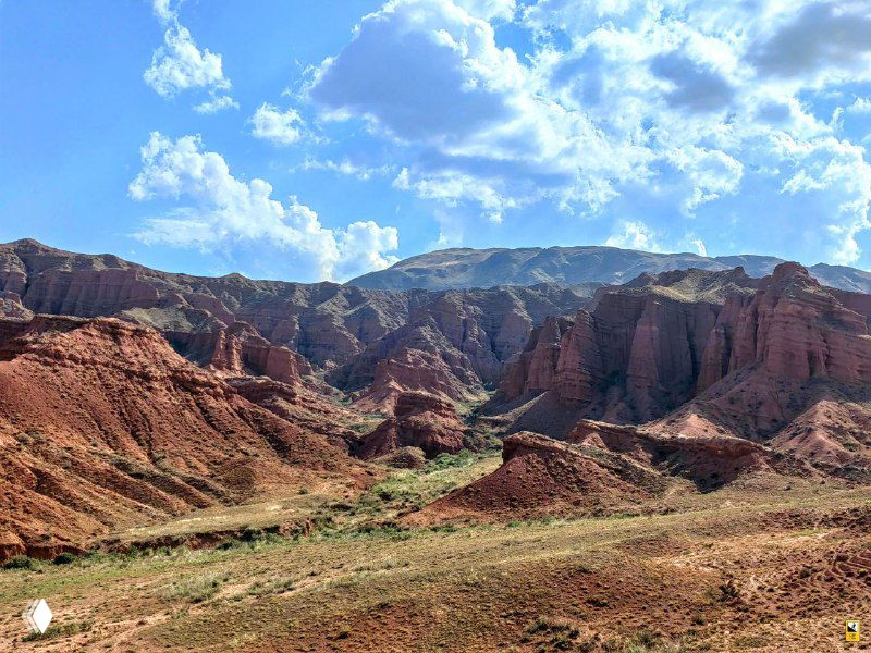 Панорамный вид на узкую ложбину между красными башнями каньона Конорчек; кустарник и бесплодная почва на переднем плане.