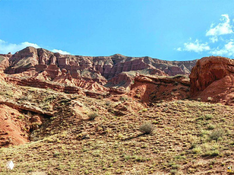 Склоны каньона с редкой травянистой растительностью и ржавыми оттенками пород — вид на пологий подъём тропы.