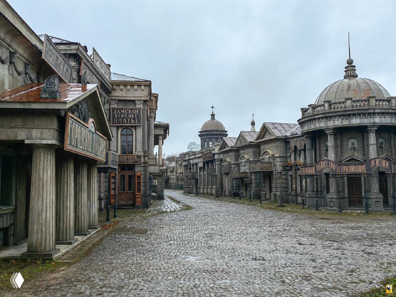 Широкий вид на брусчатую улицу декораций с рядом зданий по обе стороны: пустая площадь и ровные линии архитектуры студийного Петербурга.