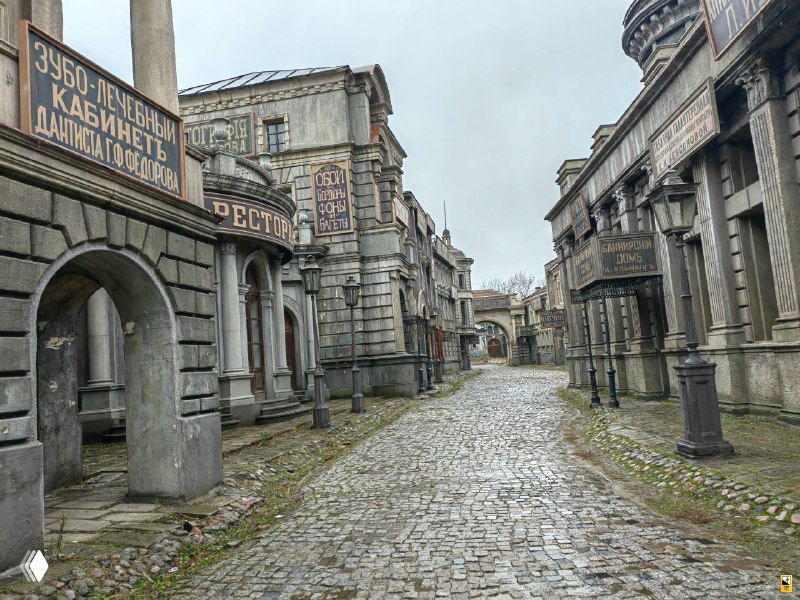 Перспектива пустой брусчатой улицы между фанерными домами — глубокий план декораций, имитирующих петербургские кварталы без современных элементов.