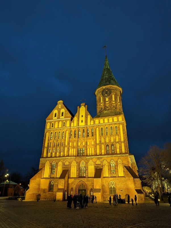 Ночное освещение фасада Кафедрального собора в Калининграде: крупный план подсвеченного кирпичного готического фасада и входной части здания.