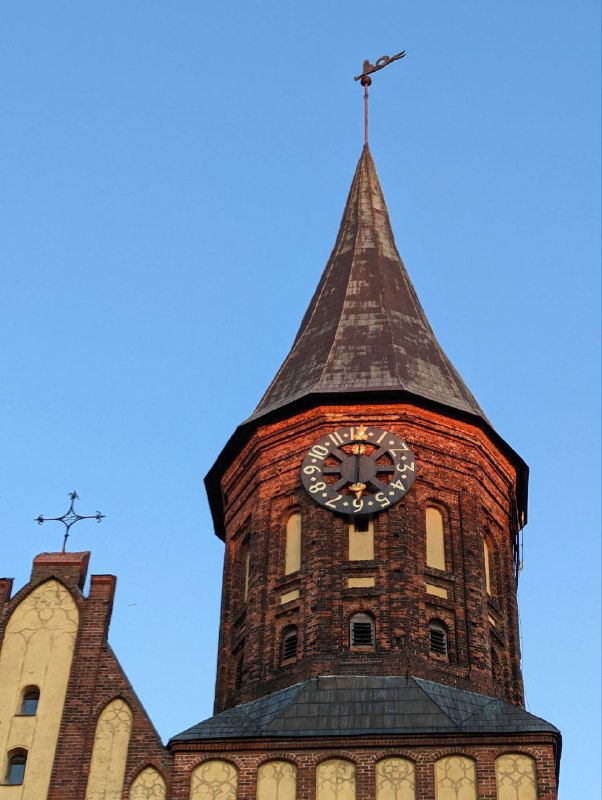 Часовая башня собора Канта крупным планом на фоне голубого неба, видна старинная кирпичная кладка и циферблат часов на башне.