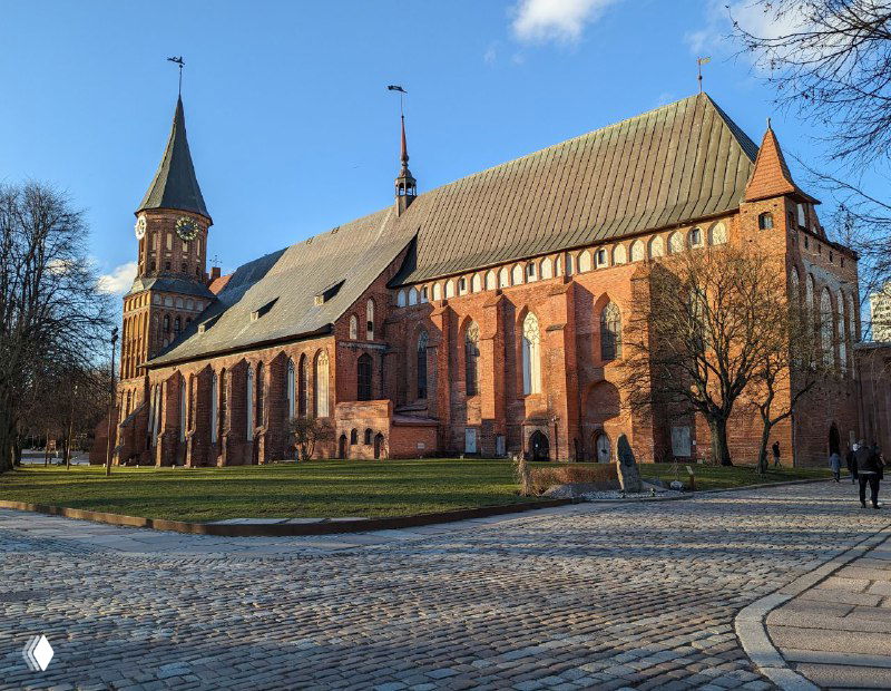 Фронтальный вид на Кафедральный собор днем: кирпичная готическая архитектура, парк вокруг и мощеная передняя площадь у входа.