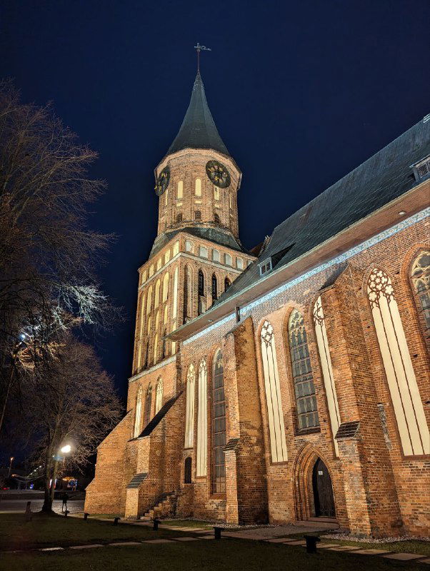 Ночной общий план собора с подсветкой и боковым ракурсом: массивные контуры, витые арки и игра света на кирпичах в темноте.