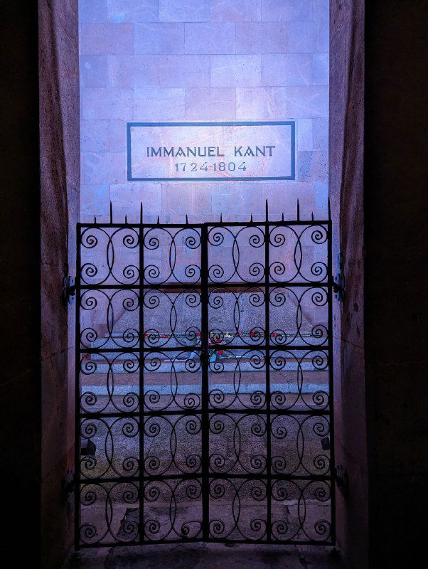 Каменная плита с надписью IMMANUEL KANT внутри мемориального пространства собора, ограждение и приглушенное освещение вокруг могилы философа.