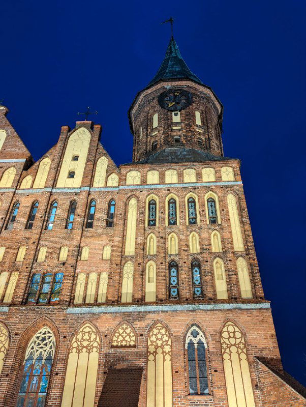 Взгляд снизу на освещенный высокий фасад Кафедрального собора вечером, видны стрельчатые окна и характерный готический силуэт башен.