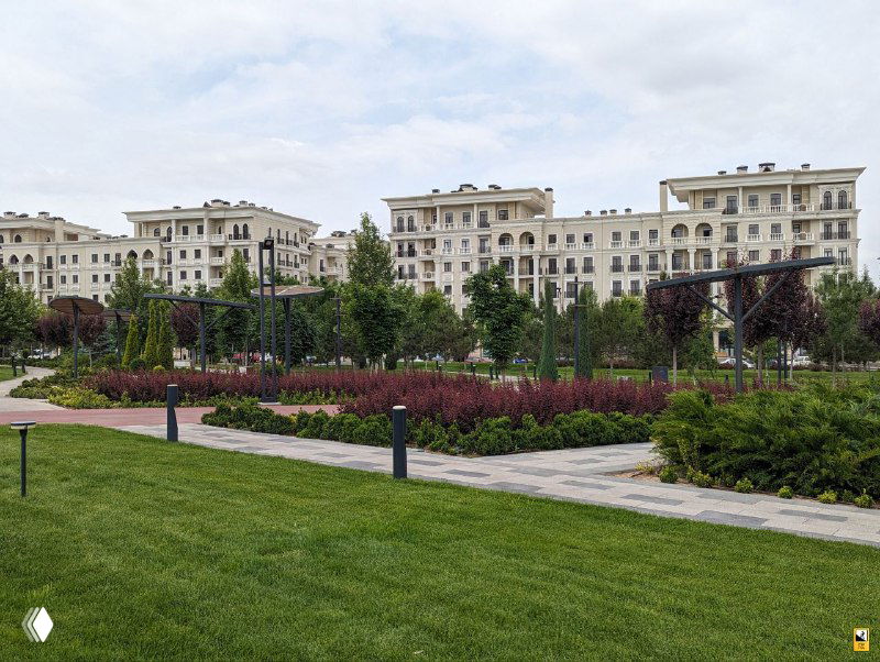 Небольшой парк перед жилыми комплексами в новом квартале Ташкента; низкоэтажные здания в европейском стиле, газоны и декоративные клумбы создают уютную атмосферу.