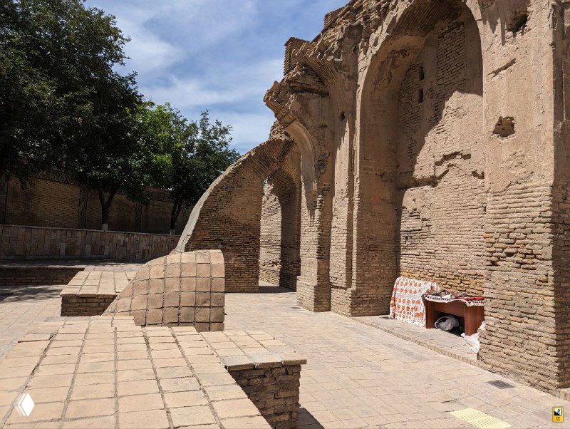Остатки и архитектурные арки рядом с комплексом: древние кирпичные структуры, руинированные элементы и светлые ступени вблизи памятника.