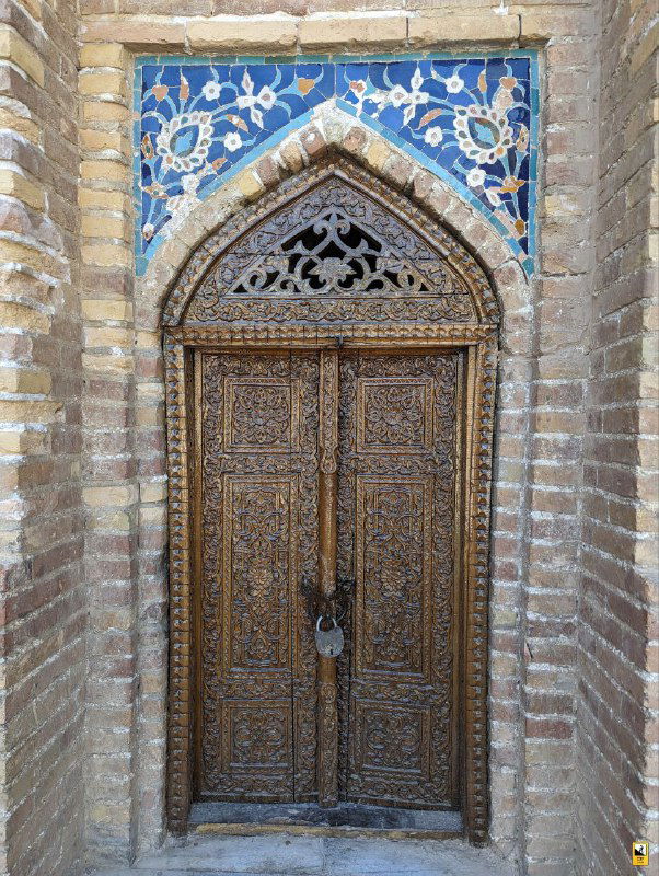 Деревянная резная дверь в одном из помещений комплекса: декоративная резьба, массивная дверная конструкция и замок в традиционном стиле.