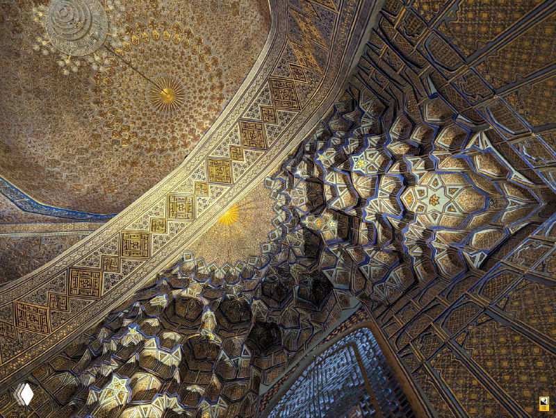 Интерьерный фрагмент купола и сводов с мукарнасами и золотисто-синими росписями: сложный орнамент и своды, подсвеченные мягким светом.