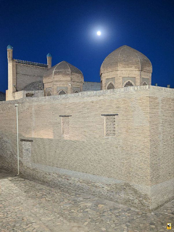 Купола и кирпичные стены исторического комплекса в Бухаре под ночным или вечерним небом; мягкий свет выделяет силуэты строений.