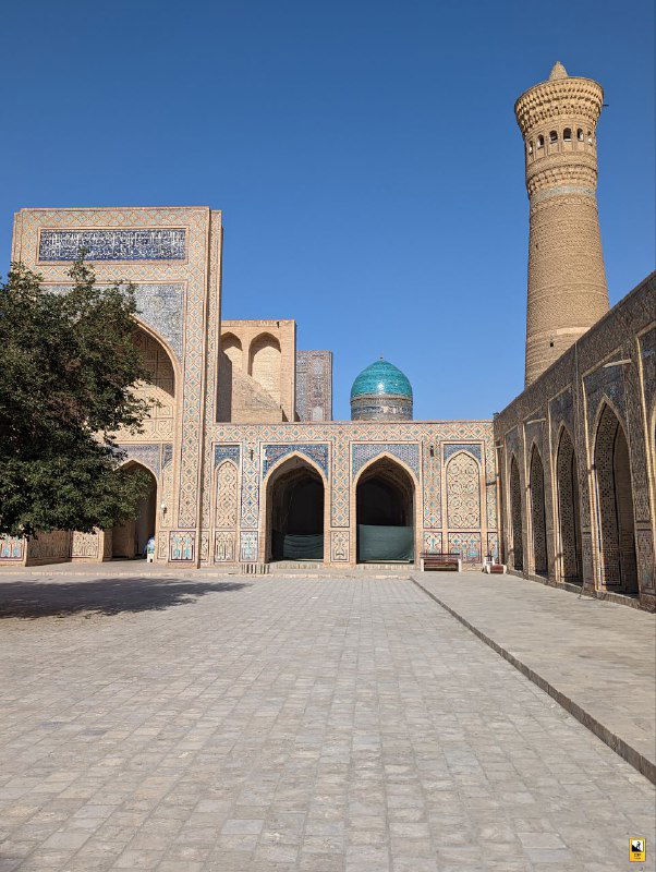 Внутренний двор медресе или мечети в Бухаре: открытая площадь с аркадой, минарет и голубые купола на фоне чистого неба.