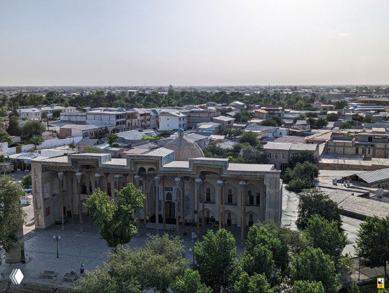 Панорамный вид на кварталы Бухары с высоты башни: низкие дома, купола мавзолеев и узкие улицы под ровным светом.